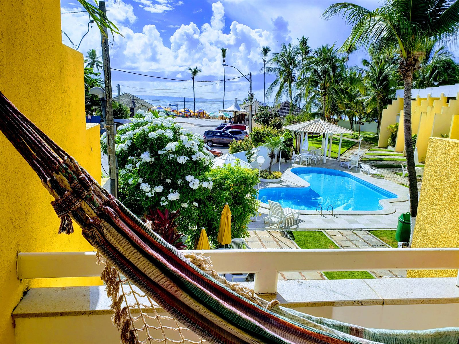 Vista da varanda com rede, piscina do condomínio e o mar ao fundo